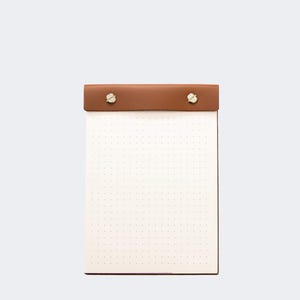 Könnte beinhalten: Ein kleiner Notizblock mit Punktraster, braunem Lederaufsatz und goldfarbenen Schrauben. Der Notizblock hat ein weißes Papierinnere mit kleinen, gleichmäßig verteilten Punkten. Der Notizblock ist rechteckig und steht aufrecht vor weißem Hintergrund.