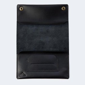 Puede incluir: Una cartera de cuero negro con cierre de solapa y un peque&ntilde;o bolsillo en la parte delantera. La cartera tiene un logotipo en relieve sutil en la parte delantera.
