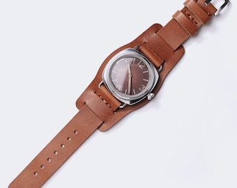 May include: A brown leather watch strap with a silver watch face. The strap has a buckle closure and is designed to fit around the wrist.