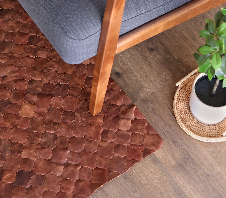 May include: A brown leather rug with a hexagonal pattern. The rug is made of individual pieces of leather that are sewn together. The rug is placed on a hardwood floor and a chair is sitting on top of it.