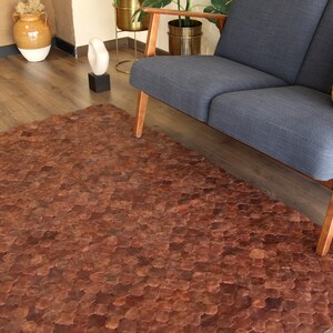 May include: A brown leather rug made of hexagonal pieces. The rug is in a living room setting with a couch and a wooden floor.