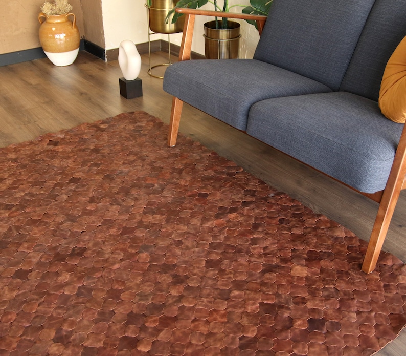 May include: A brown leather rug made of hexagonal pieces. The rug is in a living room setting with a couch and a wooden floor.