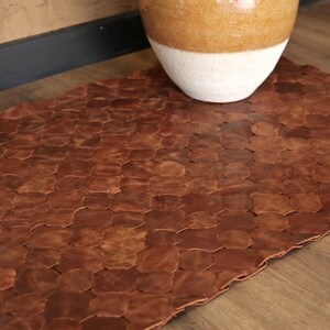 May include: A brown leather rug made of individual pieces of leather sewn together in a honeycomb pattern.