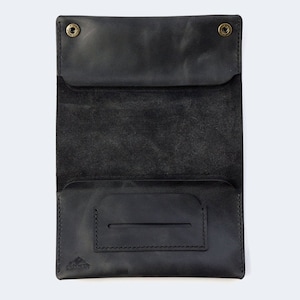 Puede incluir: Cartera de cuero negro con cierre de solapa y un peque&ntilde;o bolsillo en el interior. La cartera tiene un borde cosido y un peque&ntilde;o logotipo en la parte inferior.