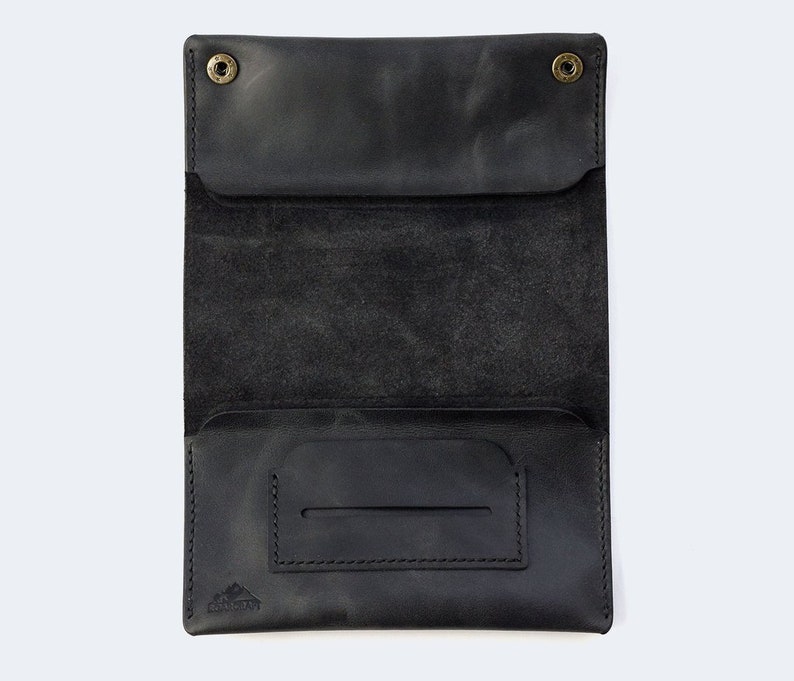 Puede incluir: Cartera de cuero negro con cierre de solapa y un peque&ntilde;o bolsillo en el interior. La cartera tiene un borde cosido y un peque&ntilde;o logotipo en la parte inferior.