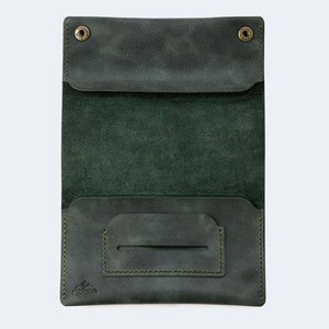 Puede incluir: Una cartera de cuero verde oscuro con dos cierres a presi&oacute;n y un bolsillo &uacute;nico en la parte delantera. La cartera est&aacute; abierta para revelar un solo bolsillo en el interior.