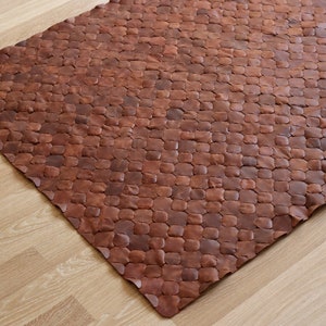 May include: A brown leather rug with a unique, textured design. The rug is made of individual pieces of leather that are sewn together to create a honeycomb pattern.