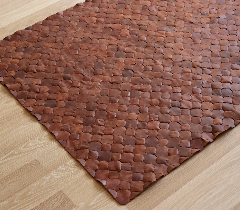 May include: A brown leather rug with a unique, textured design. The rug is made of individual pieces of leather that are sewn together to create a honeycomb pattern.