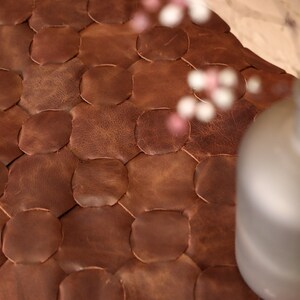 May include: Close-up of a brown leather ottoman with a honeycomb pattern. The ottoman is made of individual pieces of leather sewn together.