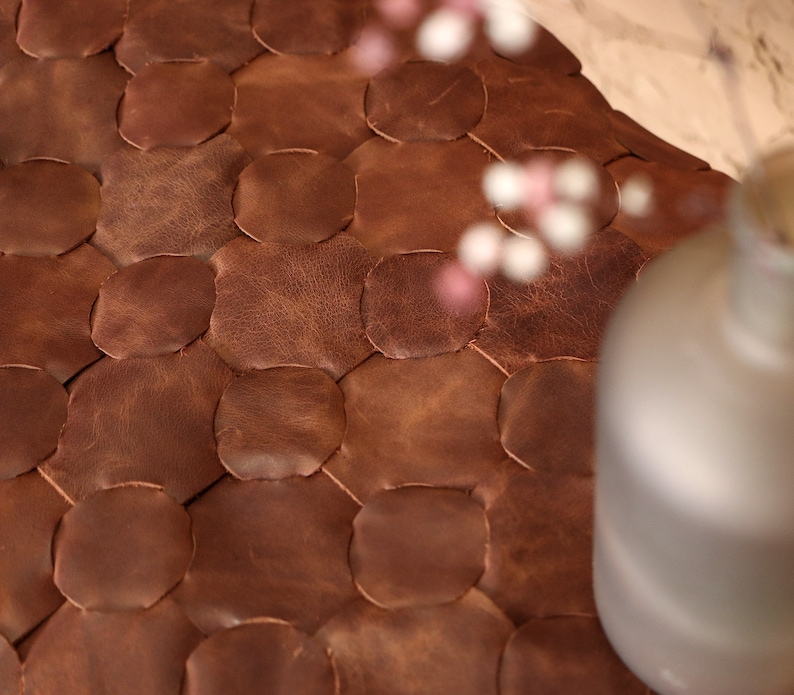 May include: Close-up of a brown leather ottoman with a honeycomb pattern. The ottoman is made of individual pieces of leather sewn together.