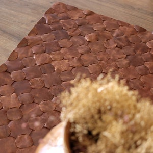 May include: A brown leather rug with a woven pattern of circles. The rug is made of individual pieces of leather that are sewn together.