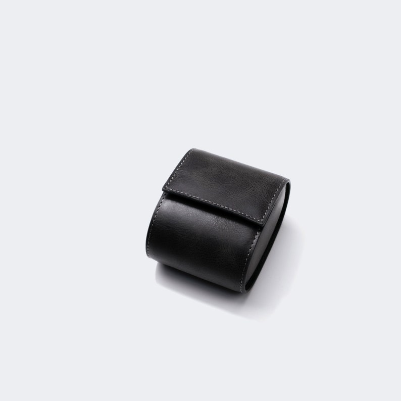 May include: A black leather watch box with a stitched seam.