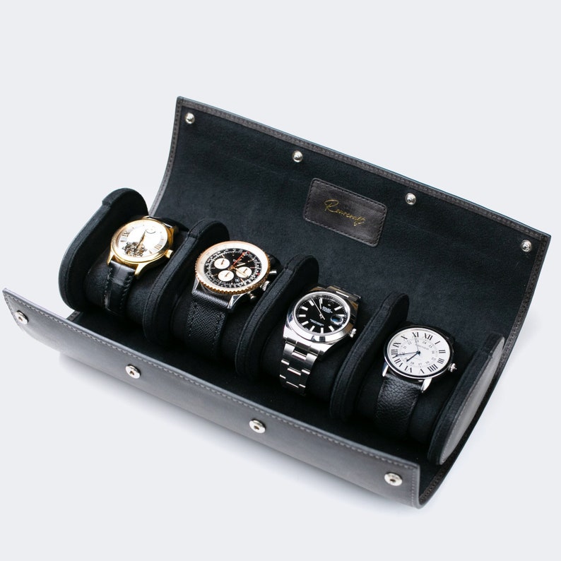 May include: A black leather watch winder with five slots for watches. The winder is open and shows four watches with different styles and colors. The winder has the word "Remarkable" embossed on the inside.
