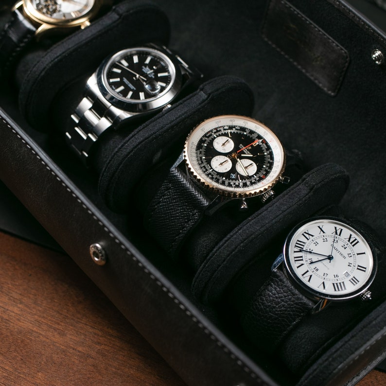 May include: A black leather watch box with four watch winders. Each winder has a black leather strap and a different watch with a silver, gold, or black face.