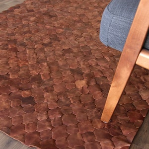 May include: A brown leather rug with a hexagonal pattern. The rug is made of individual pieces of leather that are sewn together.