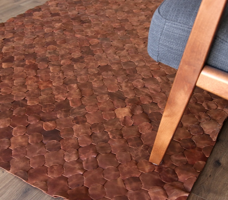 May include: A brown leather rug with a hexagonal pattern. The rug is made of individual pieces of leather that are sewn together.
