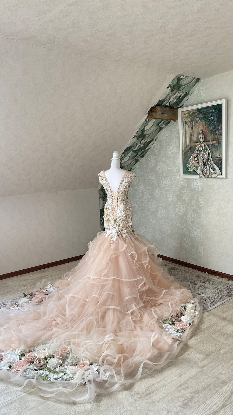 Puede incluir: Un vestido de novia de tul rosa claro con un corpi&ntilde;o ajustado y una falda completa. El corpi&ntilde;o est&aacute; adornado con delicados apliques florales y lentejuelas. La falda presenta m&uacute;ltiples capas de tul y una cola larga.