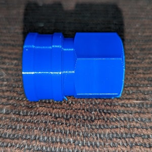May include: A bright blue, cylindrical plastic connector with a ridged design. The connector has a hexagonal shape on one end and a smaller, circular opening on the other. The object is likely a plumbing or mechanical component.