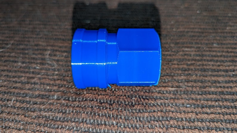 May include: A bright blue, cylindrical plastic connector with a ridged design. The connector has a hexagonal shape on one end and a smaller, circular opening on the other. The object is likely a plumbing or mechanical component.