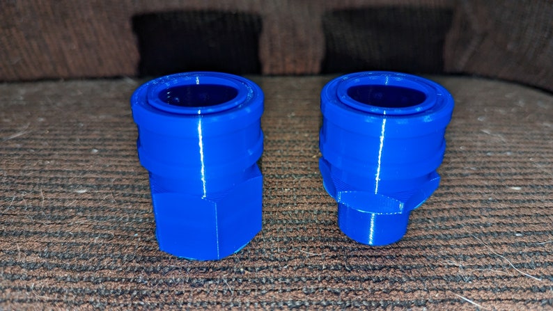 May include: Two bright blue, 3D-printed plastic connectors. One is a hexagonal shape, the other has a rounded base. Both have a circular opening at the top. The connectors are likely for plumbing or other mechanical applications.