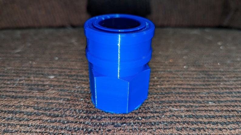 May include: A vibrant blue, 3D-printed connector with a hexagonal base and a cylindrical top. The connector has a ridged design and a hollow center. The object is likely used for plumbing or mechanical applications.