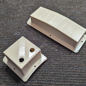 May include: Two beige plastic boxes with different shapes and sizes. The larger box has a rectangular shape with a slightly curved top and a textured surface. The smaller box has a square shape with a slightly curved top and a textured surface. Both boxes have small holes on the top.