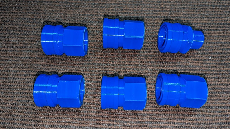 May include: Six bright blue, plastic quick-connect fittings arranged on a textured brown surface. Each fitting has a hexagonal body with a circular opening on each end. The fittings are designed for connecting hoses or tubes.