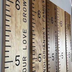 hand routed wooden growth chart rulers hanging on the wall for display, 5 boards are showing that have all been personalized and the photo shows the engraved inch marks, numbers and personalization that is superbly hand crafted with a hand router