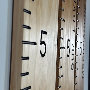 May include: Wooden growth chart with black markings and the number 5 in a bold font. The chart has black metal staples marking the height increments. The words "OUR LOVE" and a name are visible on the side of the chart.