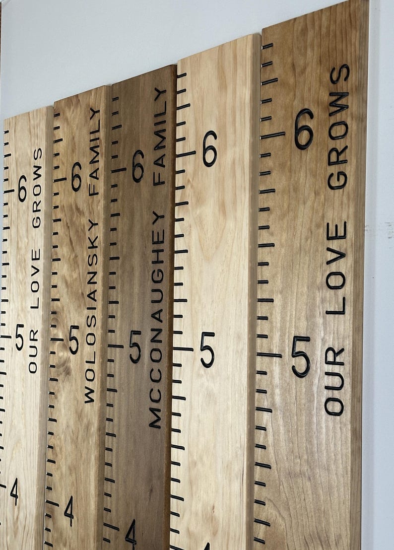 May include: Wooden growth charts with black engraved markings and text. The charts display measurements and family names, including "OUR LOVE GROWS" and "WOLOSIANSKY FAMILY". The wood has varying tones.