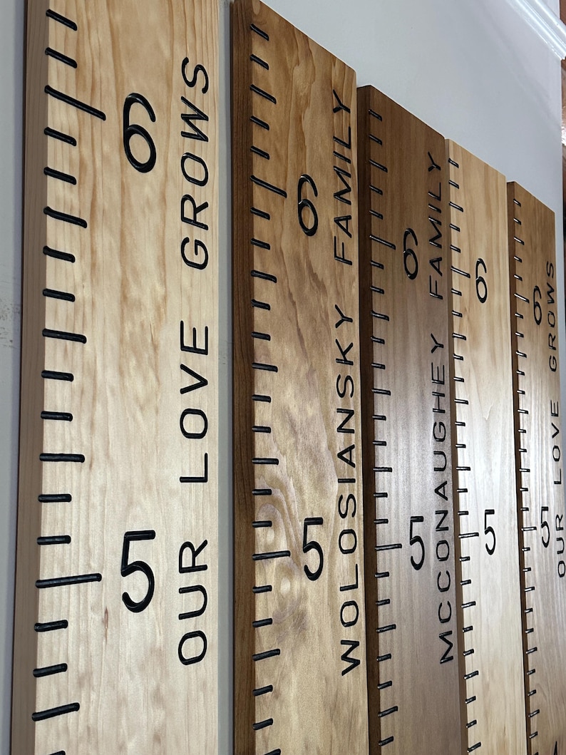 hand routed wooden growth chart rulers hanging on the wall for display, 5 boards are showing that have all been personalized and the photo shows the engraved inch marks, numbers and personalization that is superbly hand crafted with a hand router