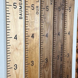 May include: Wooden growth charts in various wood tones, including Natural and Golden Oak. Each chart features family names and measurement markings in inches, from 1 to 6 feet. A decorative and functional home decor item.