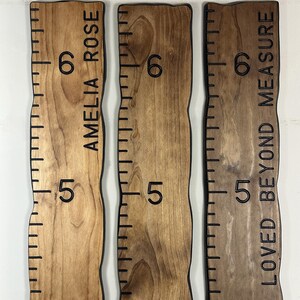 May include: Three wooden growth charts with black measurements and text. The charts are in shades of brown and have wavy edges. One chart reads "AMELIA ROSE", another reads "LOVED BEYOND MEASURE". The charts are marked with numbers 4, 5, and 6.