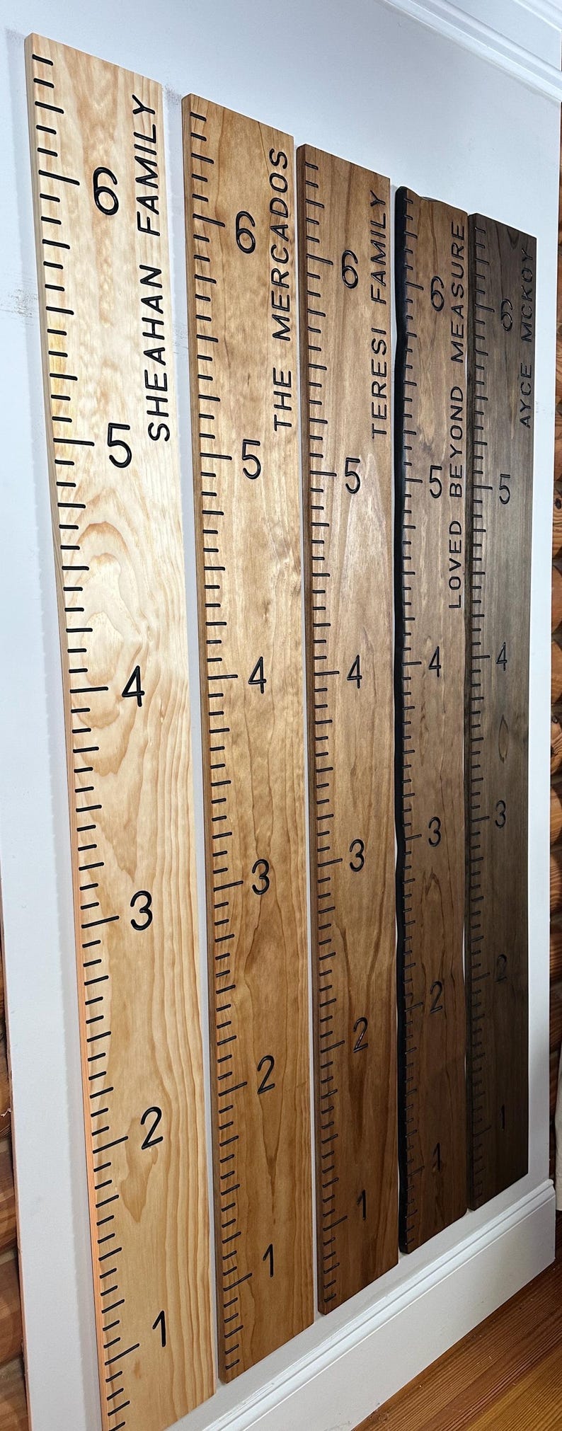 May include: Wooden growth charts with black markings and family names. The charts are in varying shades of brown and are marked with numbers and inch increments. The names "Sheahan Family", "The Mercados", "Teresi Family", "Loved Beyond Measure", and "Ayce Mckoy" are printed on the charts.