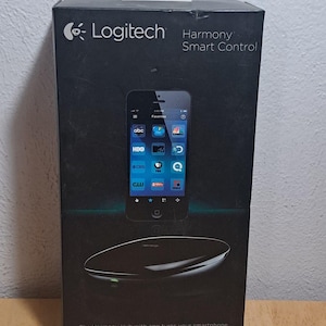 May include: A black Logitech Harmony Smart Control box featuring a smartphone display with app icons and a Harmony Hub device. The packaging includes the text Logitech Harmony Smart Control and The Harmony Hub with app turns your smartphone into a powerful universal remote.