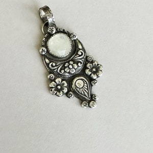 May include: A silver pendant with a moon and flower design. The pendant features a large, round, white gemstone in the center.