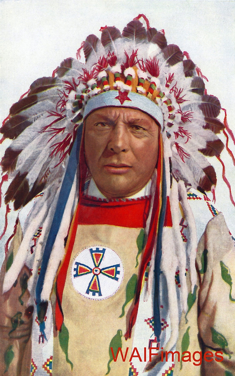 May include: Portrait of a person wearing a traditional Native American headdress and attire. The headdress features white and brown feathers, red accents, and a blue band. The attire includes a red bib and a cream-colored shirt with a circular emblem.
