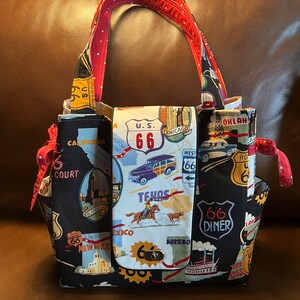 May include: A black tote bag with a red and white polka dot handle. The bag is decorated with a map of Route 66 and various landmarks along the route. The bag has a flap closure with a metal clasp.