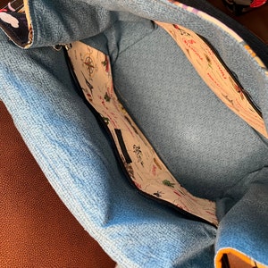 May include: The inside of a blue and white tote bag with a zippered pocket. The lining is a light blue fabric with a subtle texture. The pocket is lined with a white fabric with a map print featuring various states and cities.