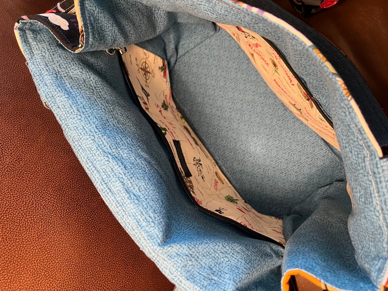 May include: The inside of a blue and white tote bag with a zippered pocket. The lining is a light blue fabric with a subtle texture. The pocket is lined with a white fabric with a map print featuring various states and cities.