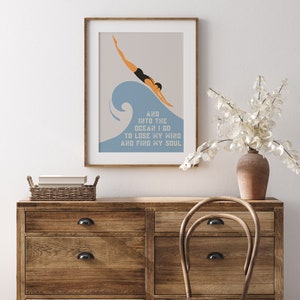 May include: A framed print with a minimalist design featuring a person diving into a blue wave. The text reads "And into the ocean I go to lose my mind and find my soul."