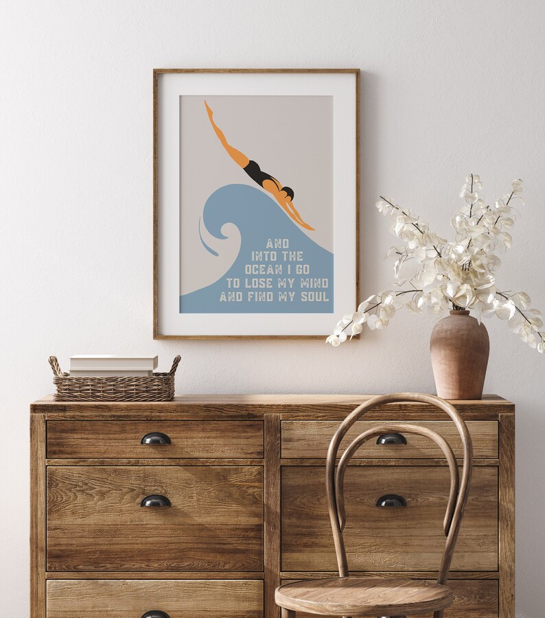 May include: A framed print with a minimalist design featuring a person diving into a blue wave. The text reads "And into the ocean I go to lose my mind and find my soul."
