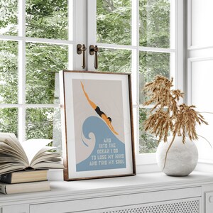 May include: A framed print with a minimalist illustration of a person diving into a blue wave. The text below the image reads "And into the ocean I go to lose my mind and find my soul."
