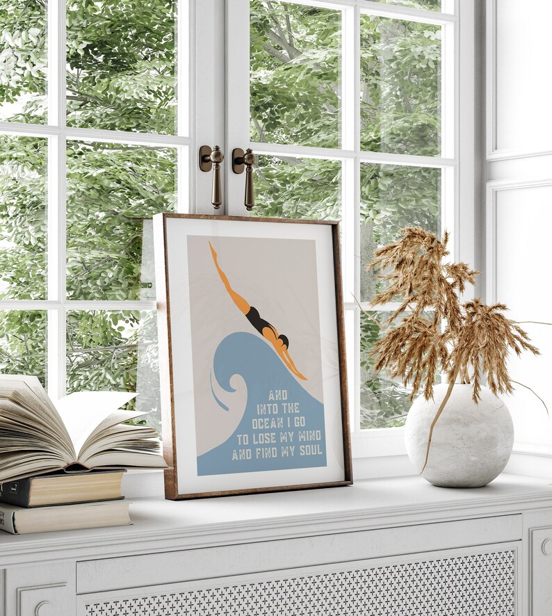 May include: A framed print with a minimalist illustration of a person diving into a blue wave. The text below the image reads "And into the ocean I go to lose my mind and find my soul."