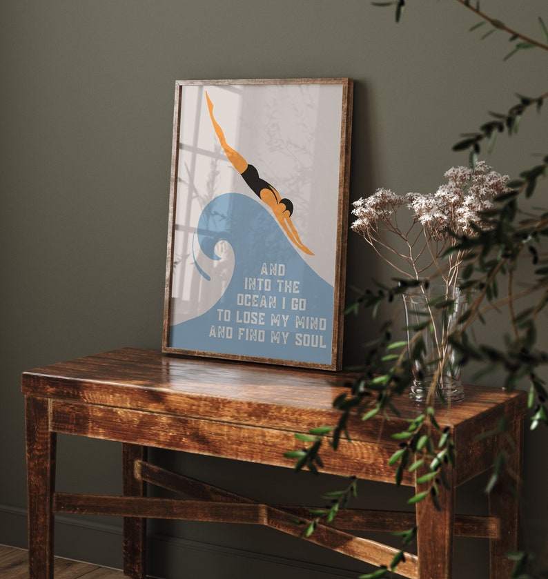 May include: A framed print with a blue and white illustration of a person diving into a wave. The text below the image reads "And into the ocean I go to lose my mind and find my soul."