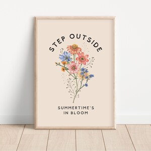 May include: A beige poster with the text "STEP OUTSIDE" in a black circular font. The text "SUMMER TIME'S IN BLOOM" is below the circle. A bouquet of pink, blue, and yellow flowers is in the center of the circle.