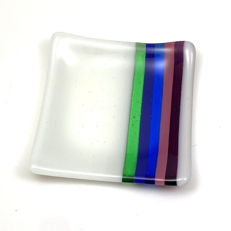 May include: A white square glass dish with a green, blue, and purple stripe design.