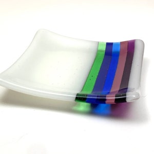 May include: A white glass dish with a curved edge and a band of green, blue, and purple stripes.