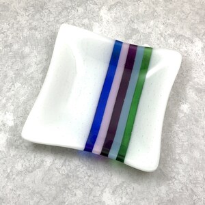 May include: A white square dish with a decorative stripe of blue, green, purple, and pink glass.