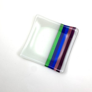 May include: A small, square, white glass dish with a decorative band of green, blue, and purple stripes.